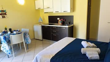 A compact hotel room with a bed, a small kitchenette, a dining table with chairs, and a single wall-mounted cabinet.