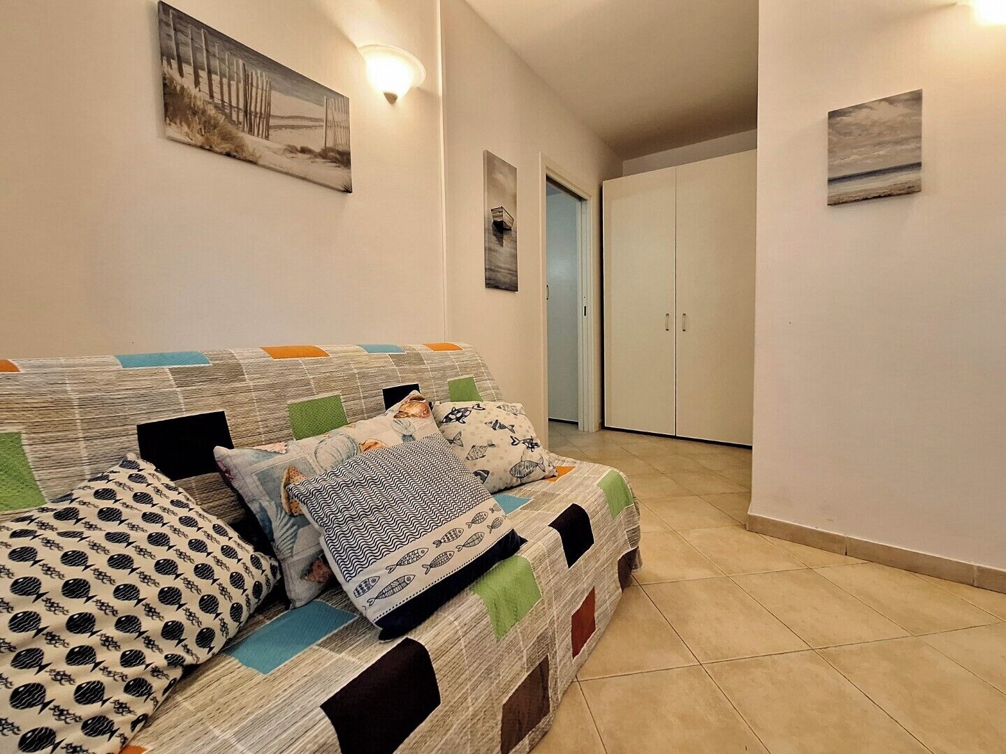 Een gezellige woonkamer met een bank, kussens en kunstwerken aan de muur.