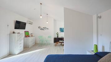 Un dormitorio moderno con una cama grande, un televisor montado en la pared y una zona de escritorio con una silla y una planta de cactus.