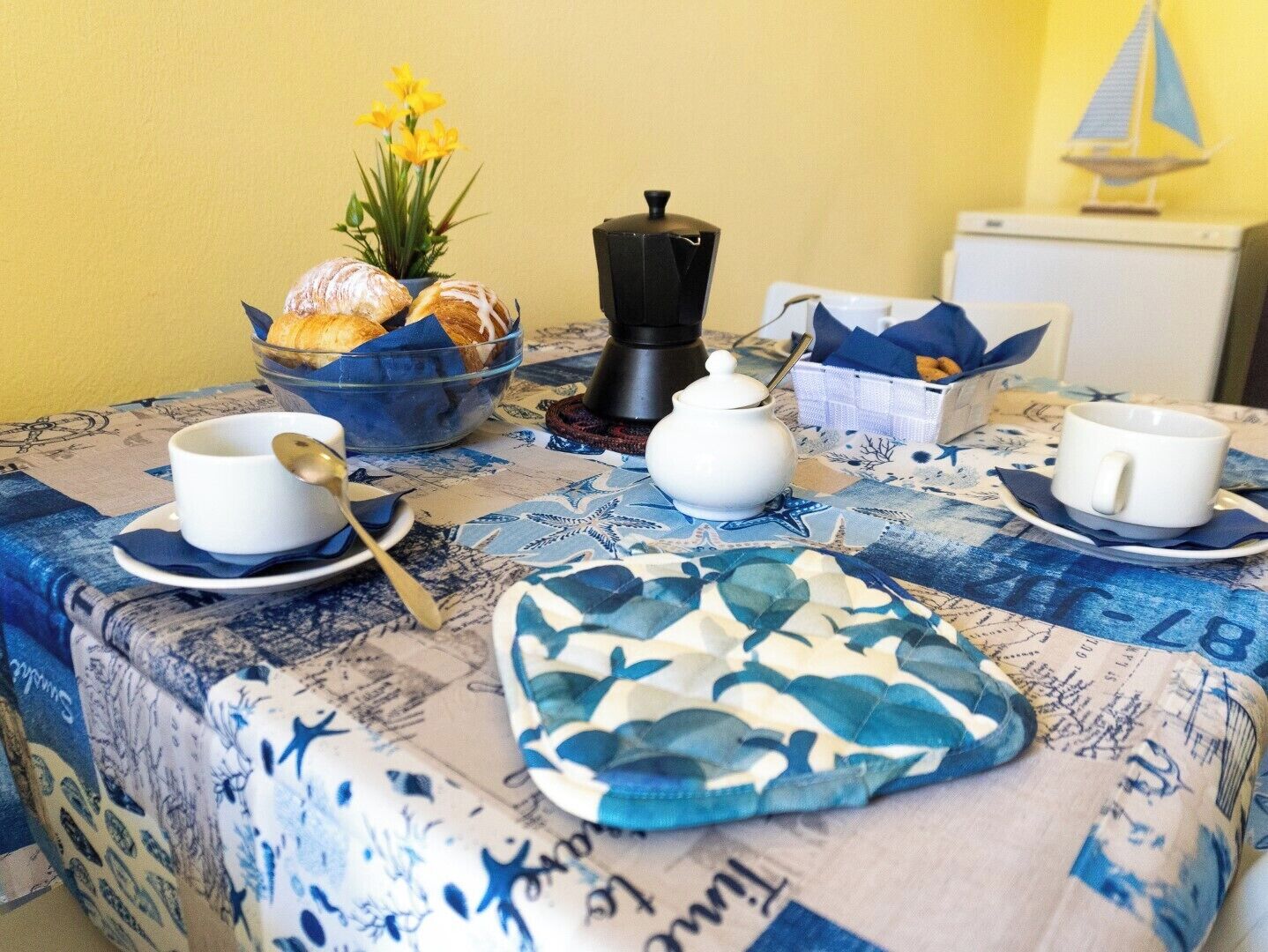 Ein Frühstückstisch mit Croissants, Kaffee und einer Tasse, bedeckt mit einer Tischdecke im maritimen Stil.