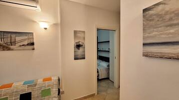 A hallway with a bed, a painting of a boat, and a painting of a beach.