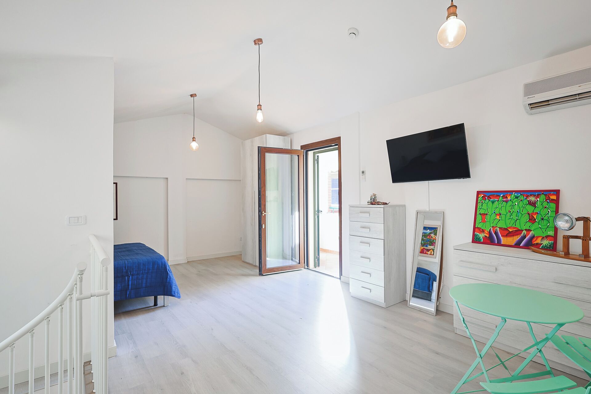 A spacious room with a bed, a desk, a chair, a TV, and a painting on the wall.