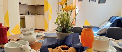 Una disposición para el desayuno con una taza de café, una tetera, un tarro de mermelada, una cesta de galletas y una planta en maceta.