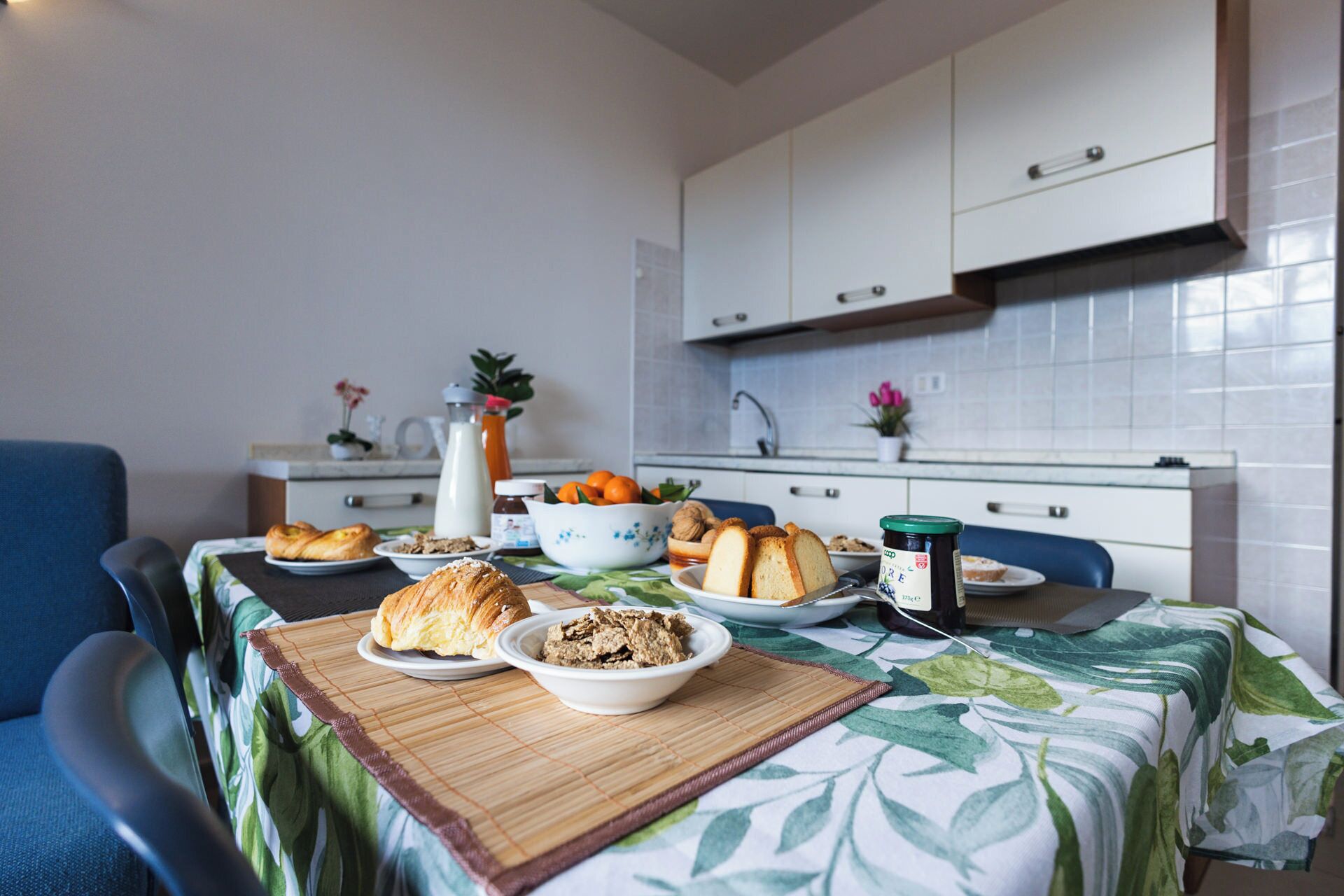 A dining area with a table set for breakfast, including croissants, bread, and a bowl of cereal.