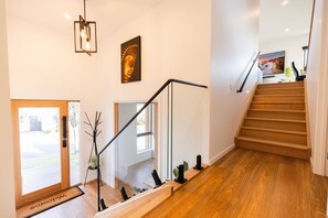 Un escalier avec des marches en bois menant à l’étage supérieur, un luminaire moderne et une œuvre d’art encadrée accrochée au mur.