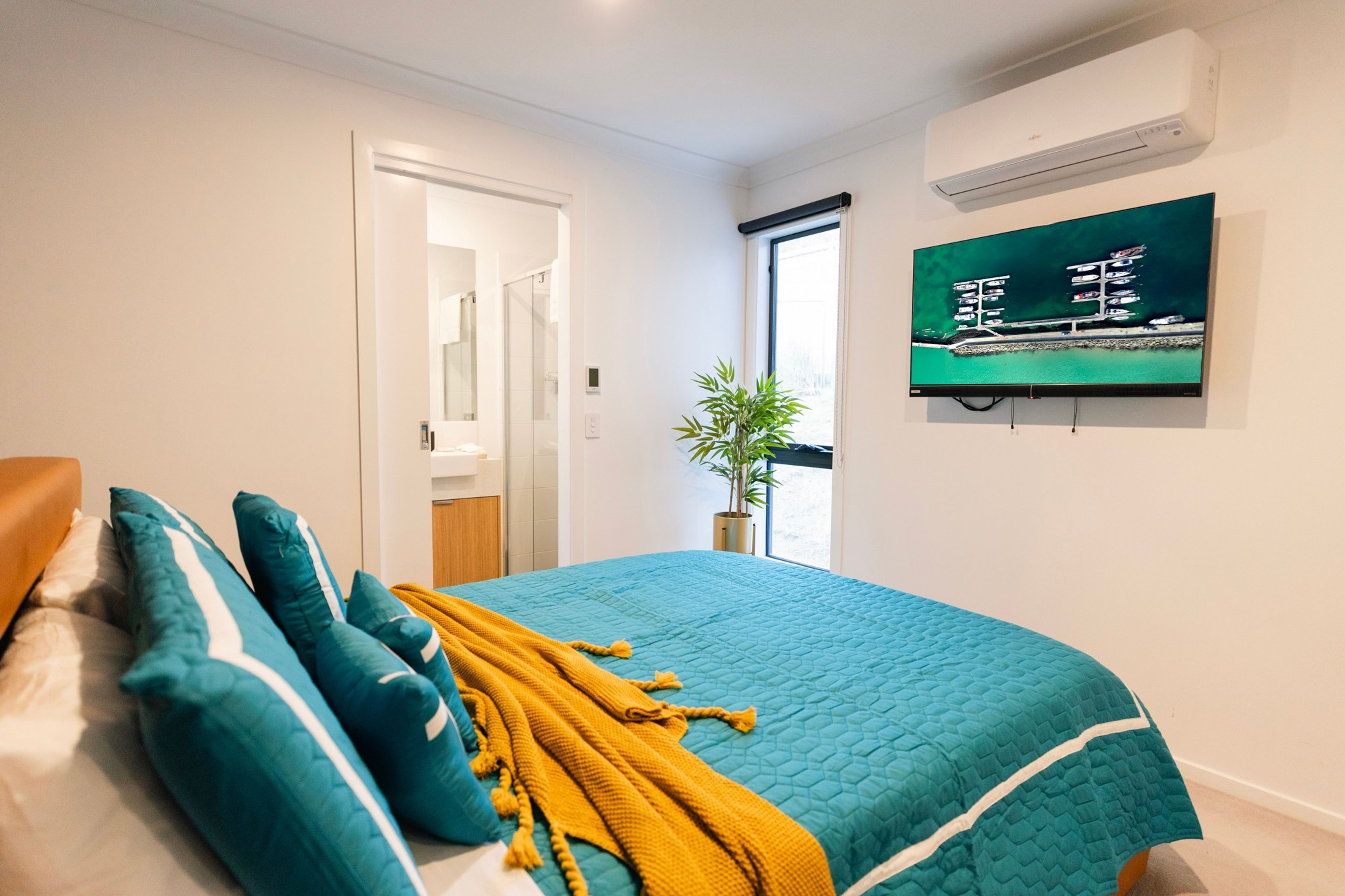 Un dormitorio con cama, almohadas, una colcha, televisión y ventana con vista a barcos.