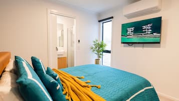 Un dormitorio con cama, almohadas, una colcha, televisión y ventana con vista a barcos.