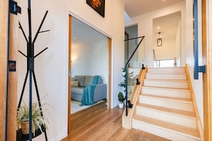 A staircase leading to a second floor, a living room with a sofa and a plant, and a coat rack with a plant.