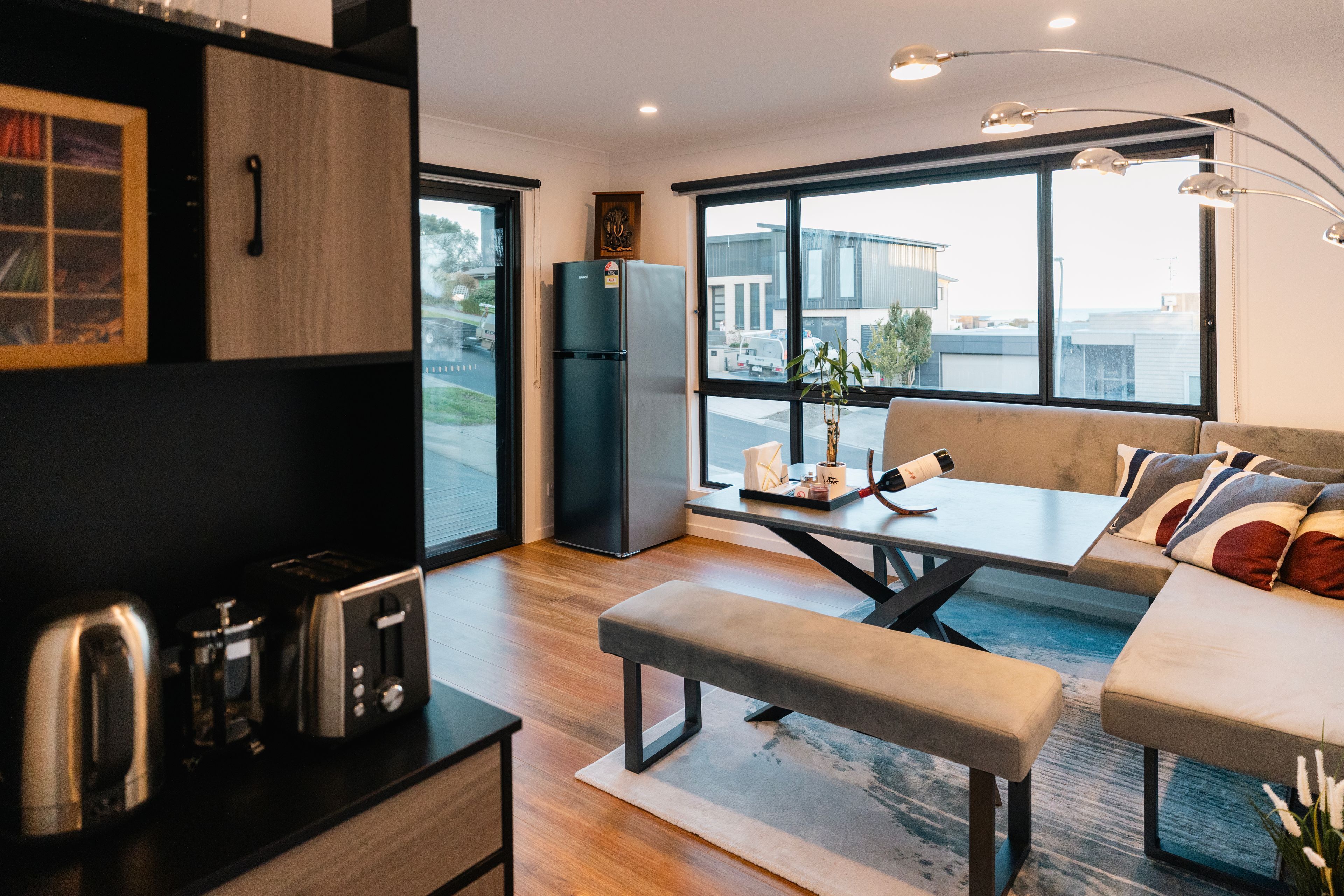 A modern kitchen with a built-in oven, a refrigerator, and a dining area with a bench and table.