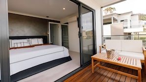 A bedroom with a bed, a sliding glass door leading to a balcony with a table and a chair.
