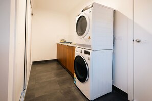 Un espace buanderie comprenant une machine à laver et un sèche-linge superposés, un meuble en bois et un sol carrelé.
