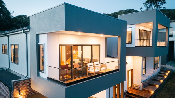 A modern two-story house with a balcony, large windows, and a staircase leading to the upper level.