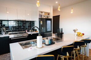 Une cuisine moderne dotée d’un îlot central, d’appareils électroménagers en acier inoxydable et d’un dosseret en carreaux noirs.
