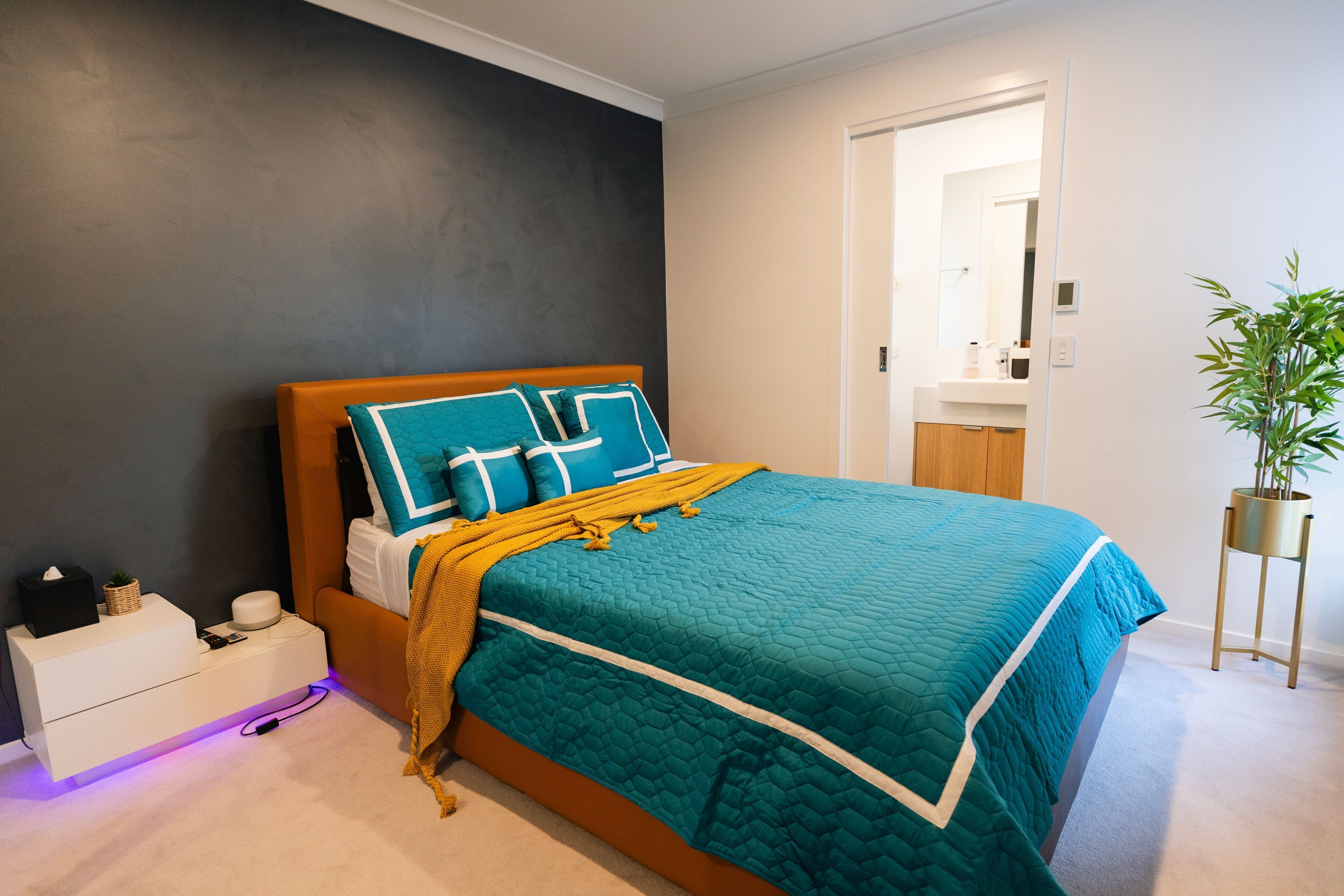 Une chambre à coucher avec un lit, une table de chevet, une commode et une plante en pot.