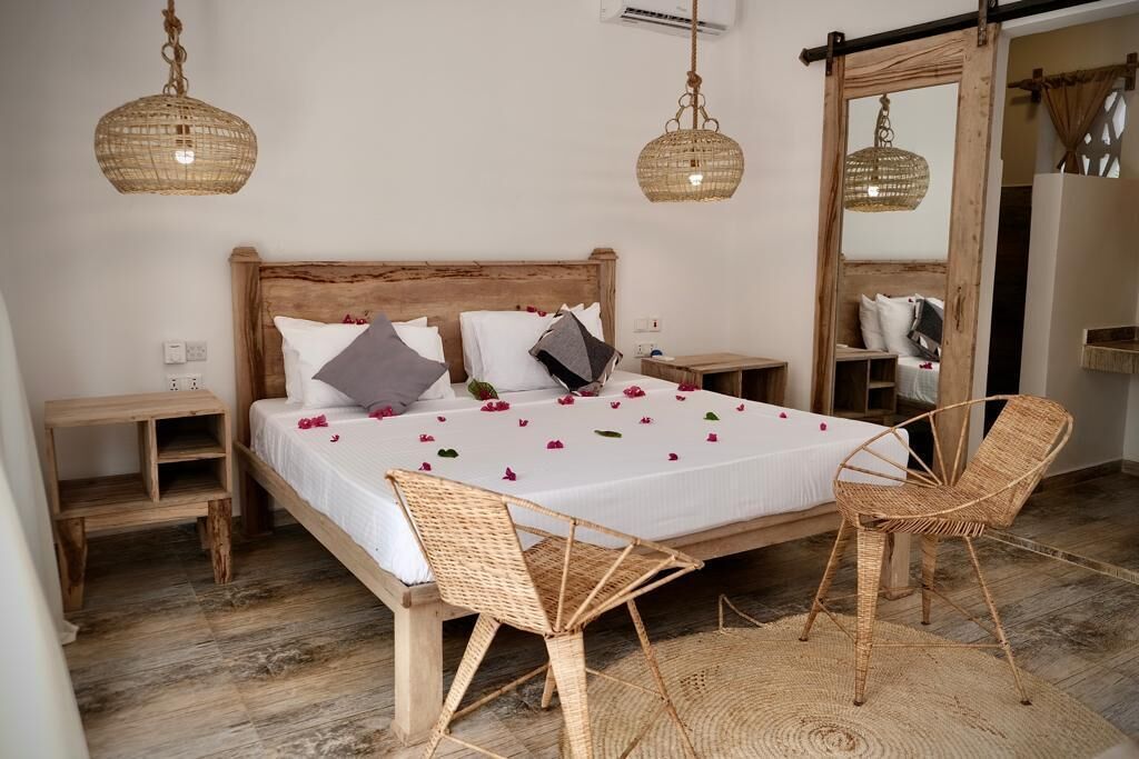 Un dormitorio con cama de madera, sillas de mimbre y un espejo grande.