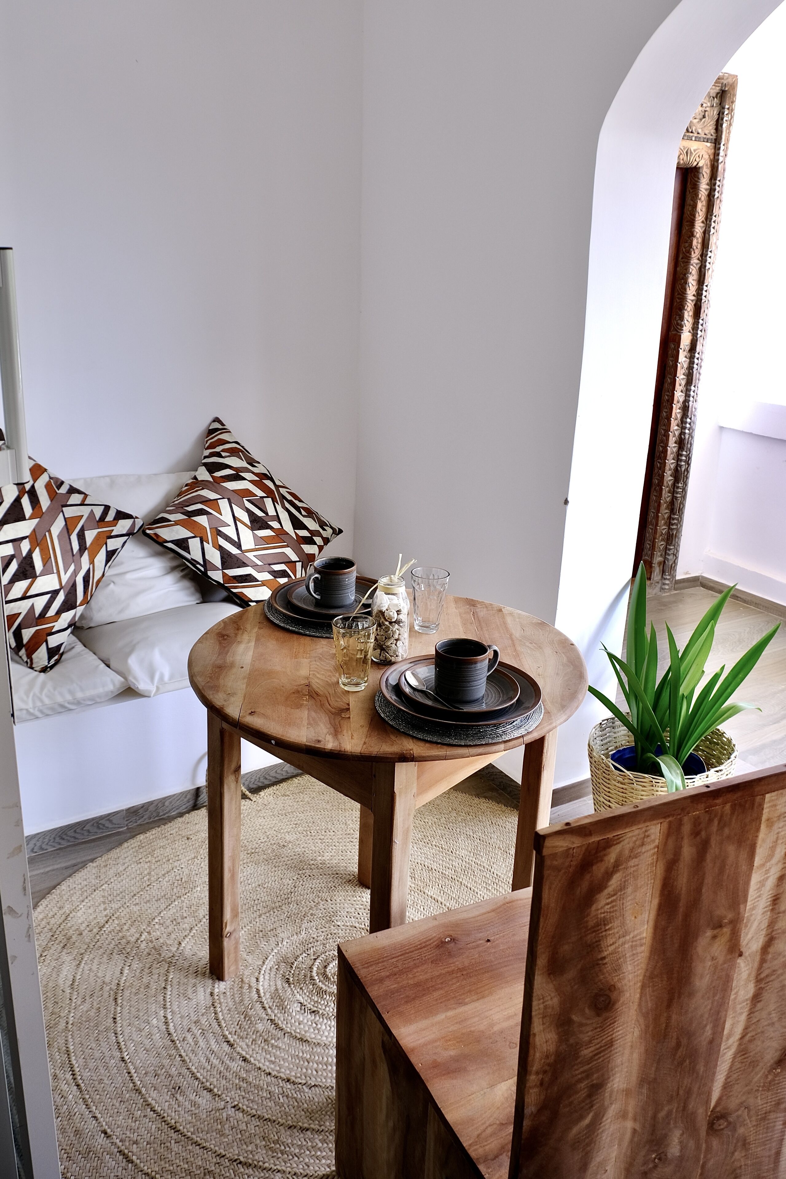 Eine Sitzecke mit Holztable und Stühlen, einem gewebten Teppich und gemusterten Kissen.