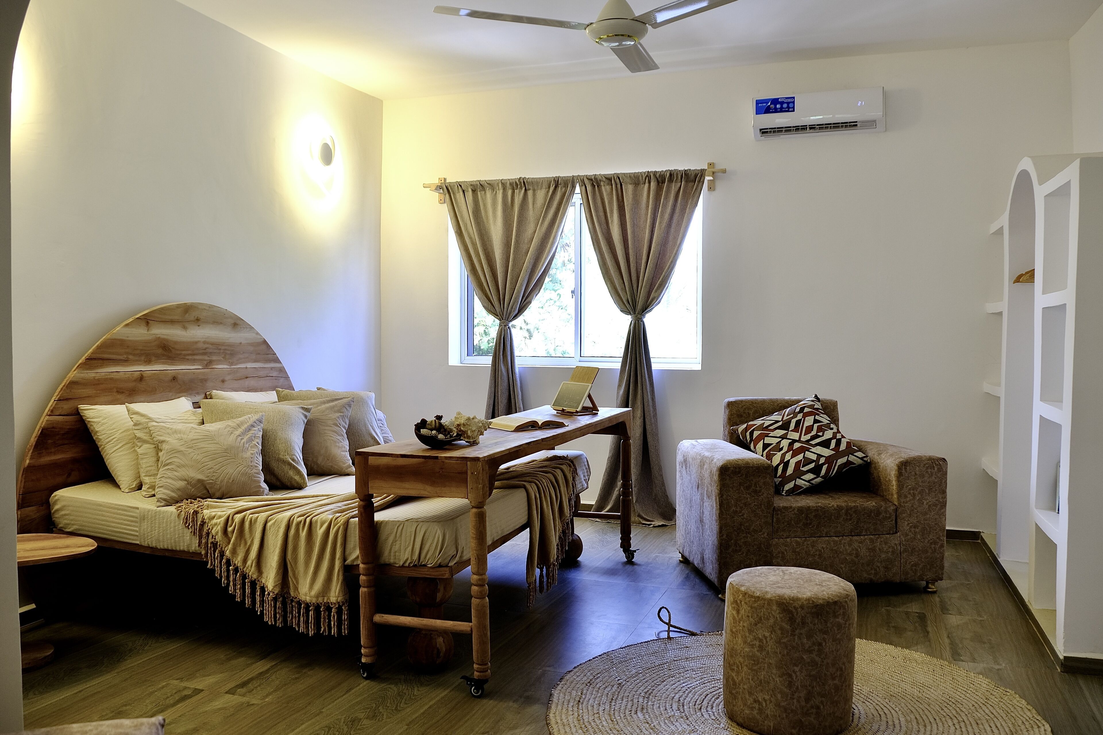 A cozy room with a wooden bed, a desk with a laptop, a chair, and a small ottoman.