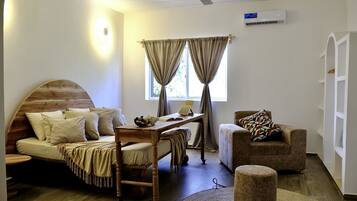 A cozy room with a wooden bed, a desk with a laptop, a chair, and a small ottoman.