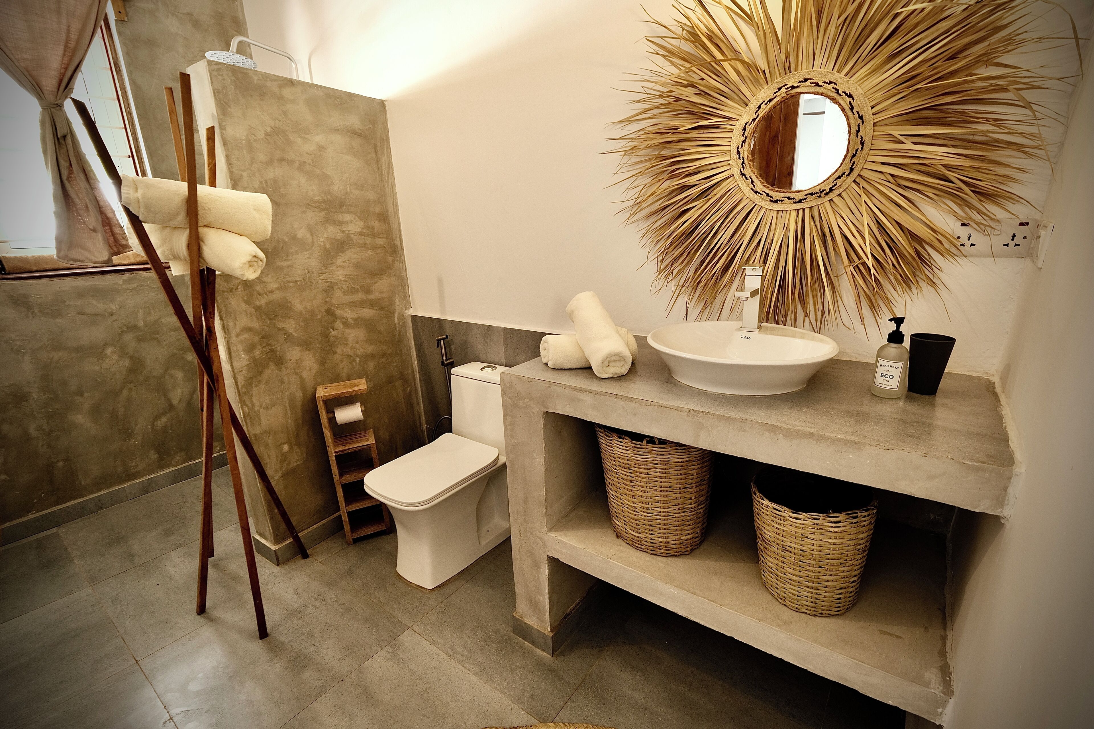 A bathroom with a concrete sink, a sunburst mirror, and a wooden towel rack.