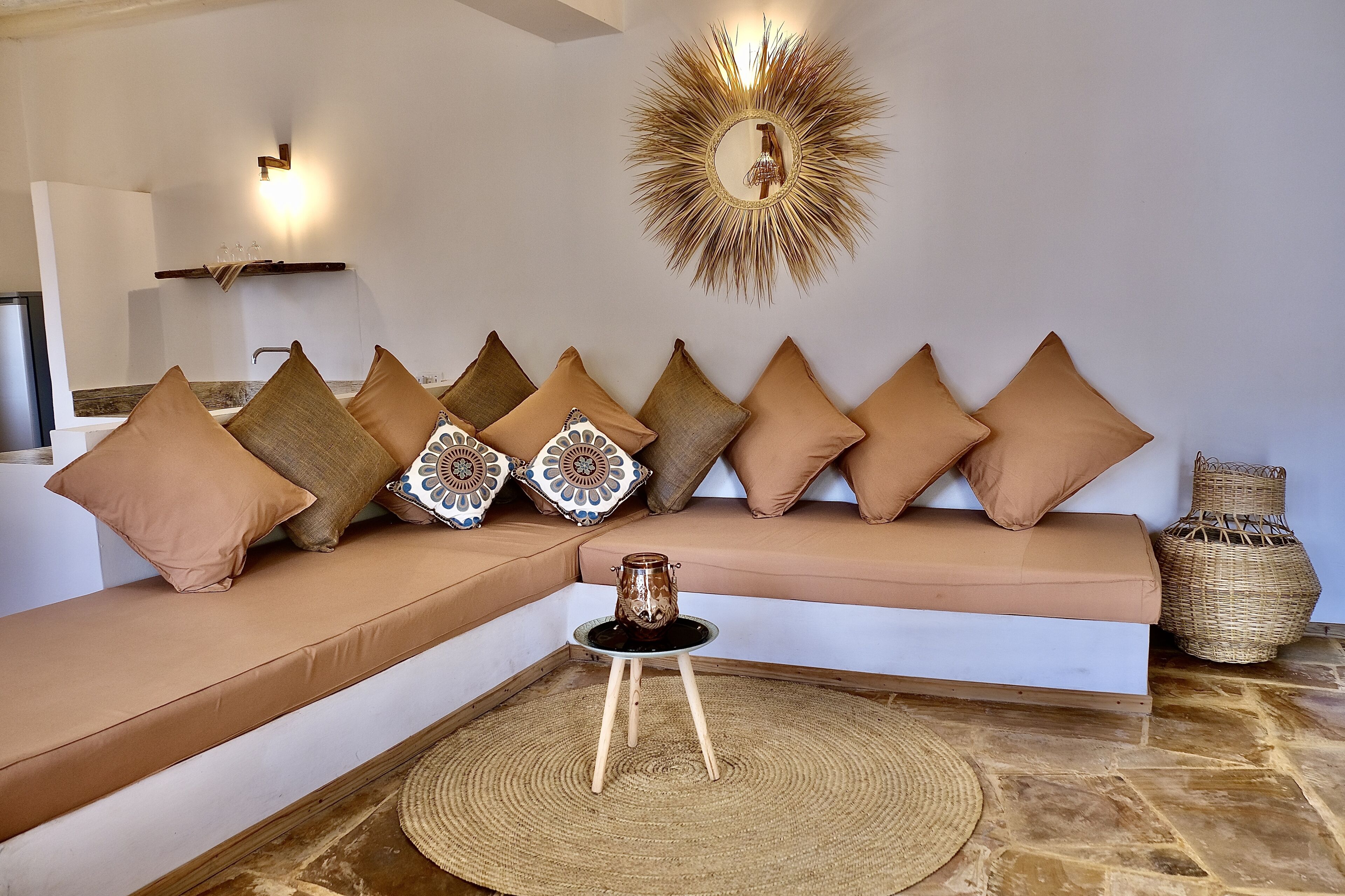 Uma sala de estar moderna com um sofá seccional, almofadas decorativas, um tapete redondo de fibra natural e um espelho fixado na parede.