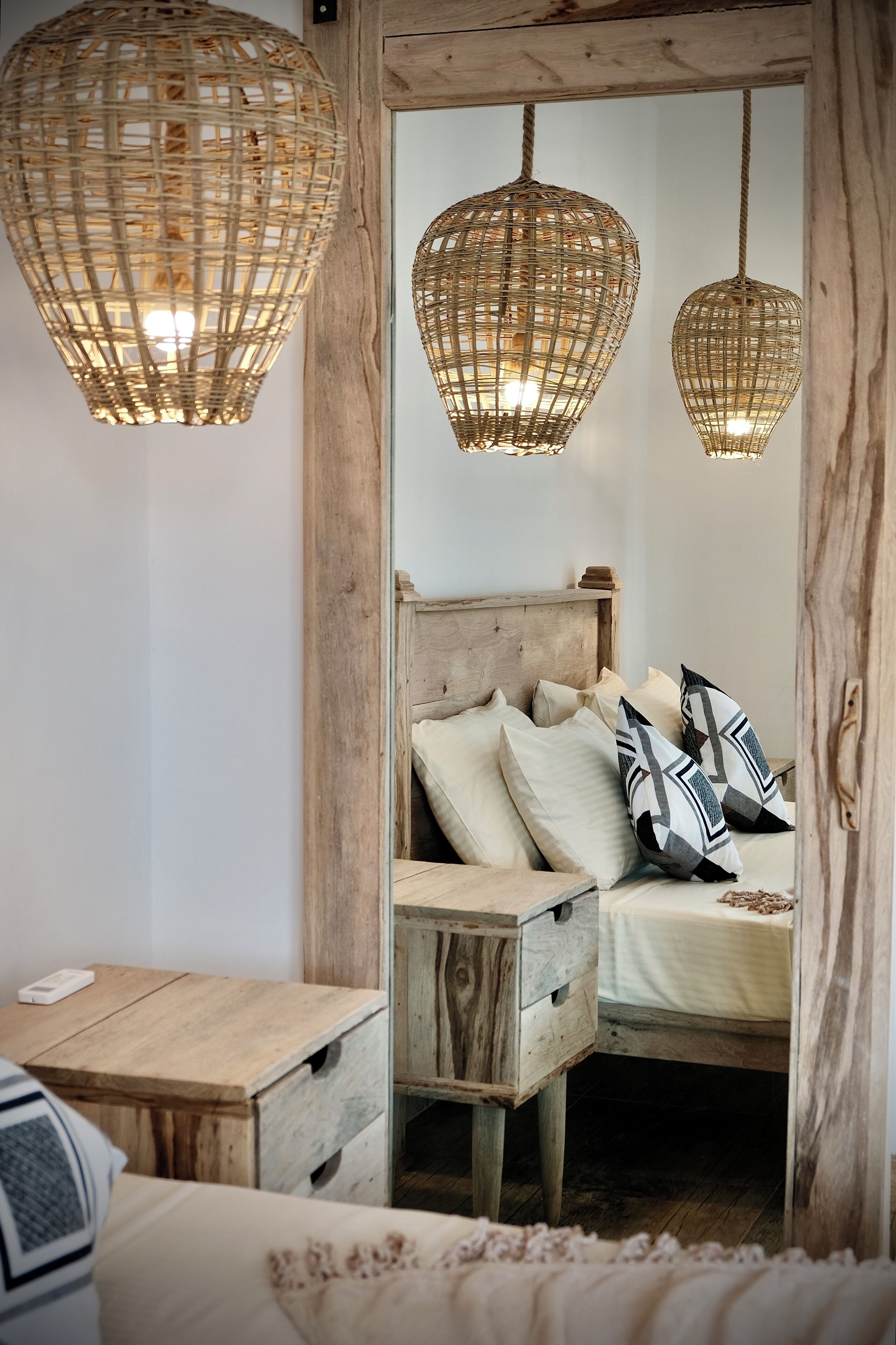 A bedroom with a wooden headboard, a wooden nightstand, and a mirror reflecting a bed with pillows.