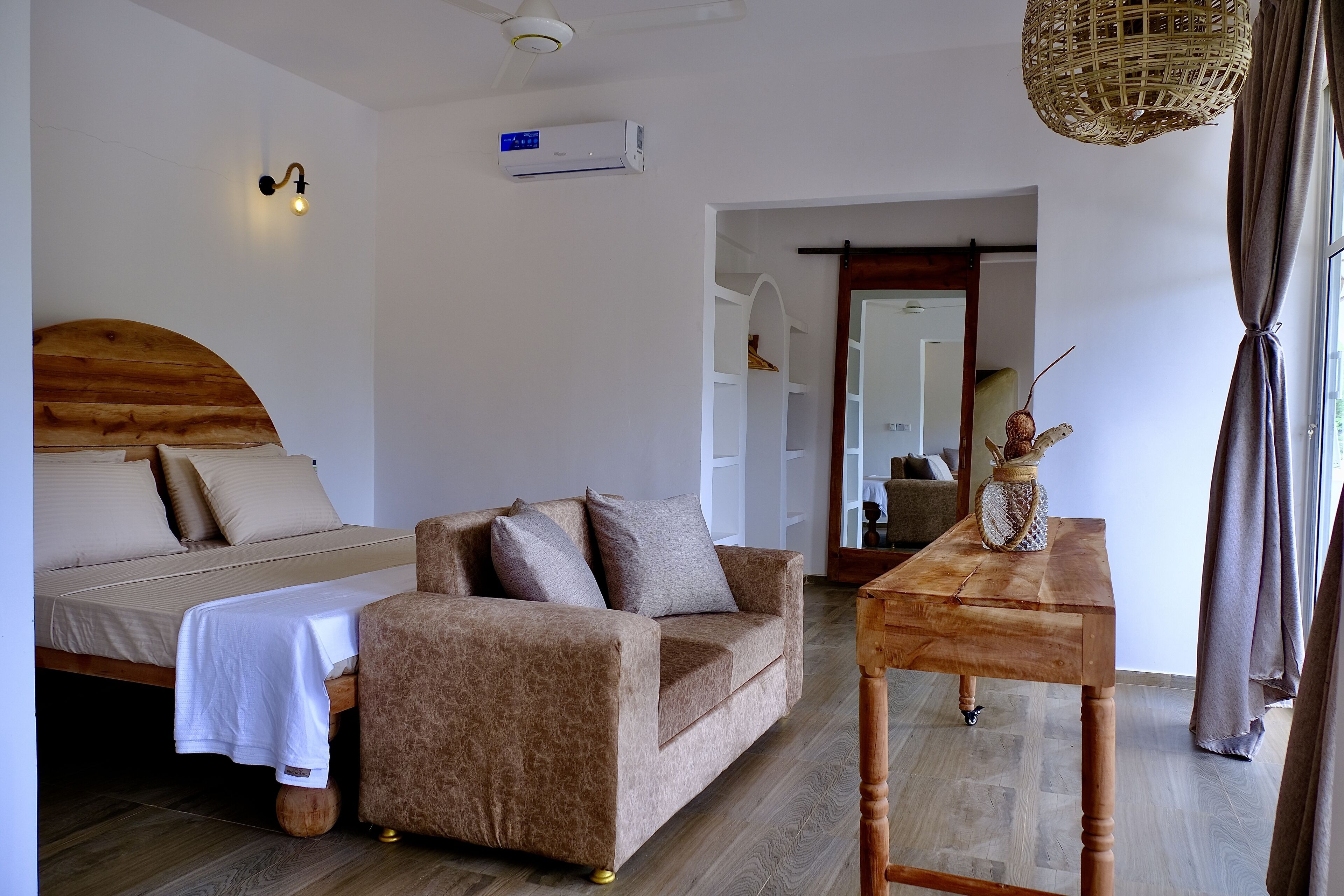 A bedroom with a bed, a sofa, a wooden table, and a ceiling fan.