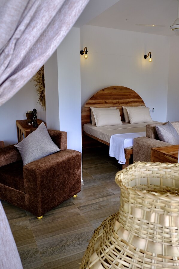 A cozy room with a bed, two brown sofas, a small table, and a wicker chair. - Antares Villa (Kiwengwa)