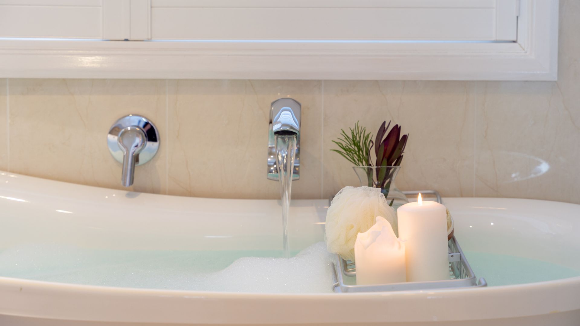 A bathtub with running water, a glass tray with candles, and a small plant.