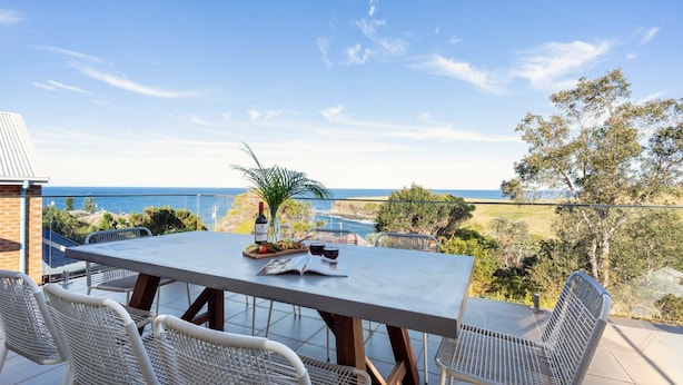 A dining table with chairs, a bottle of wine, and a menu on a terrace overlooking the ocean. - Halcyon– Breathtaking ocean views (Kiama Heights)