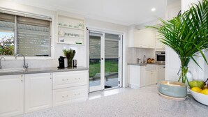 A modern kitchen with white cabinetry, a built-in oven, and a large window overlooking a garden. - Halcyon– Breathtaking ocean views (Kiama Heights)