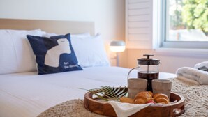 A neatly made bed with white linens, a blue pillow with a silhouette design, a coffee pot, two mugs, and a tray with croissants and a plant. - Halcyon– Breathtaking ocean views (Kiama Heights)