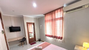 Ein Hotelzimmer mit Bett, Schreibtisch, Fernseher und einem Fenster mit Vorhängen.