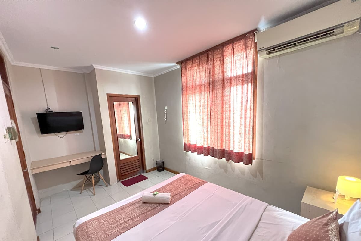 Une chambre d’hôtel avec un lit, un bureau, une télévision et une fenêtre avec des rideaux.