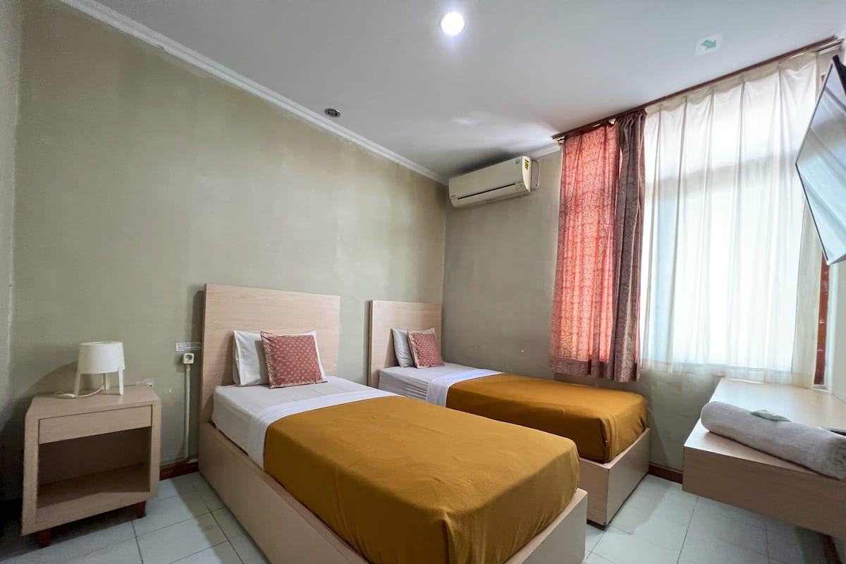 Une chambre d’hôtel avec deux lits, une table de chevet, un appareil de climatisation et une fenêtre avec des rideaux.