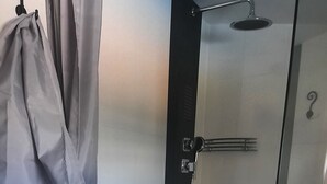 En duschkabin med glasväggar, ett handhållet duschmunstycke, en handdukshängare och en handduk som hänger på väggen.