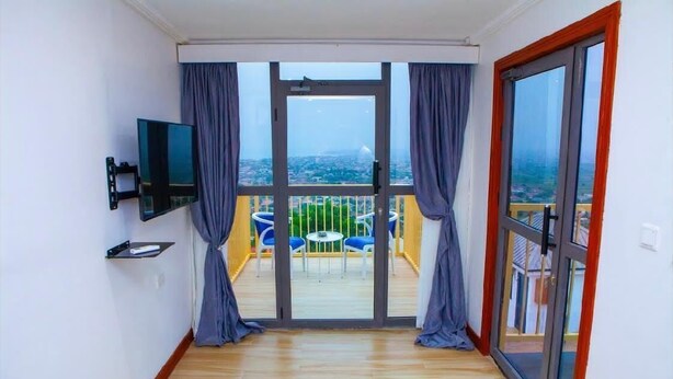 Un balcón con vistas a la ciudad, un televisor de pantalla plana en la pared y una pequeña mesa con sillas.