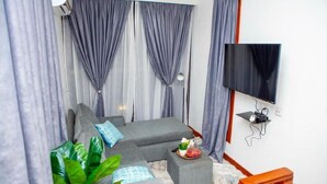 Una sala de estar moderna con un sofá gris, un televisor de pantalla plana montado en la pared y una mesita con una planta y un cuenco.
