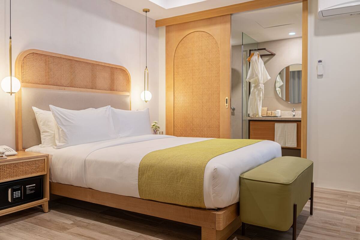 Een netjes opgemaakt bed met een houten hoofdbord, een nachtkastje met een lamp en een groene bank.