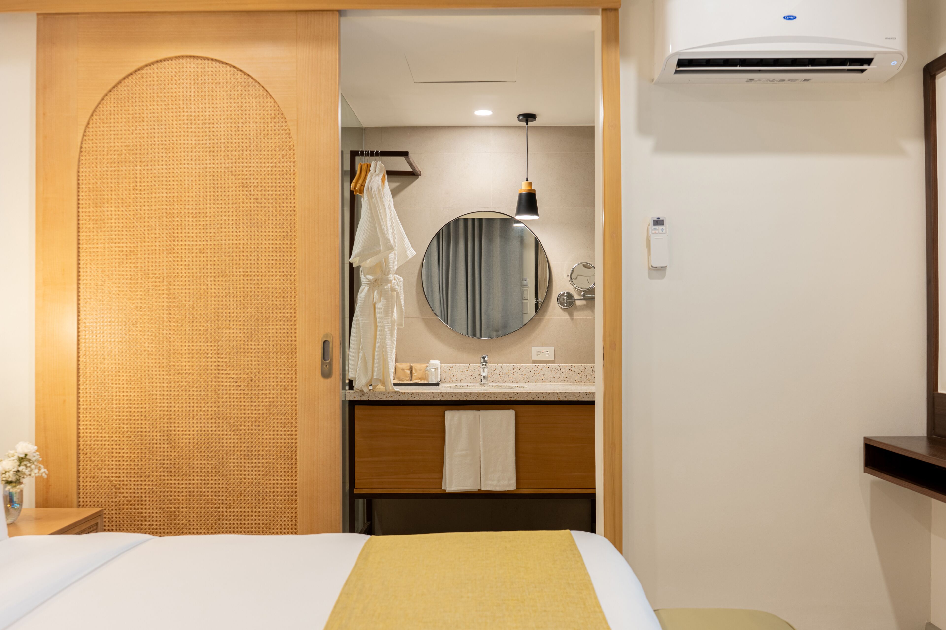 Habitación de hotel con una cama, un espejo redondo, un lavamanos y un equipo de aire acondicionado.