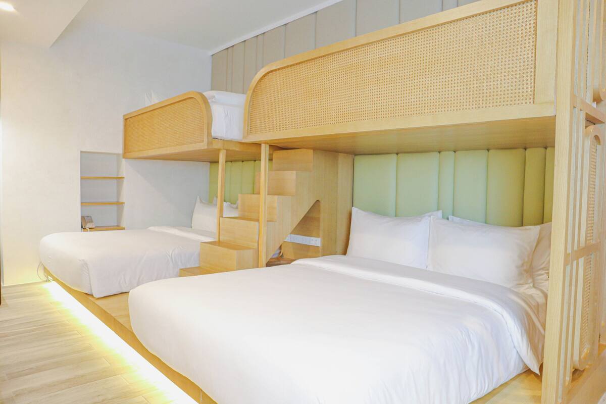 Een hotelkamer met stapelbedden, een houten trap en een neutraal kleurenpalet.