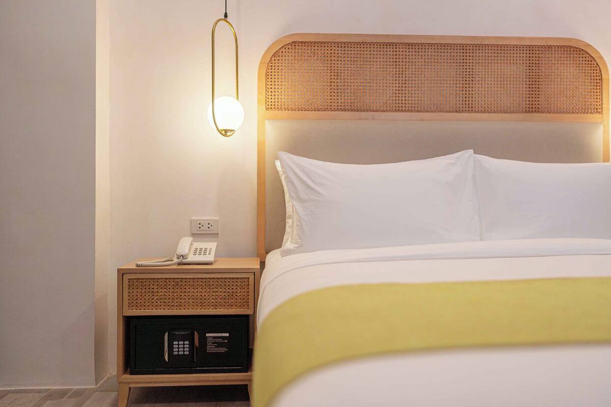 A hotel room with a bed, bedside table, lamp, and a phone.