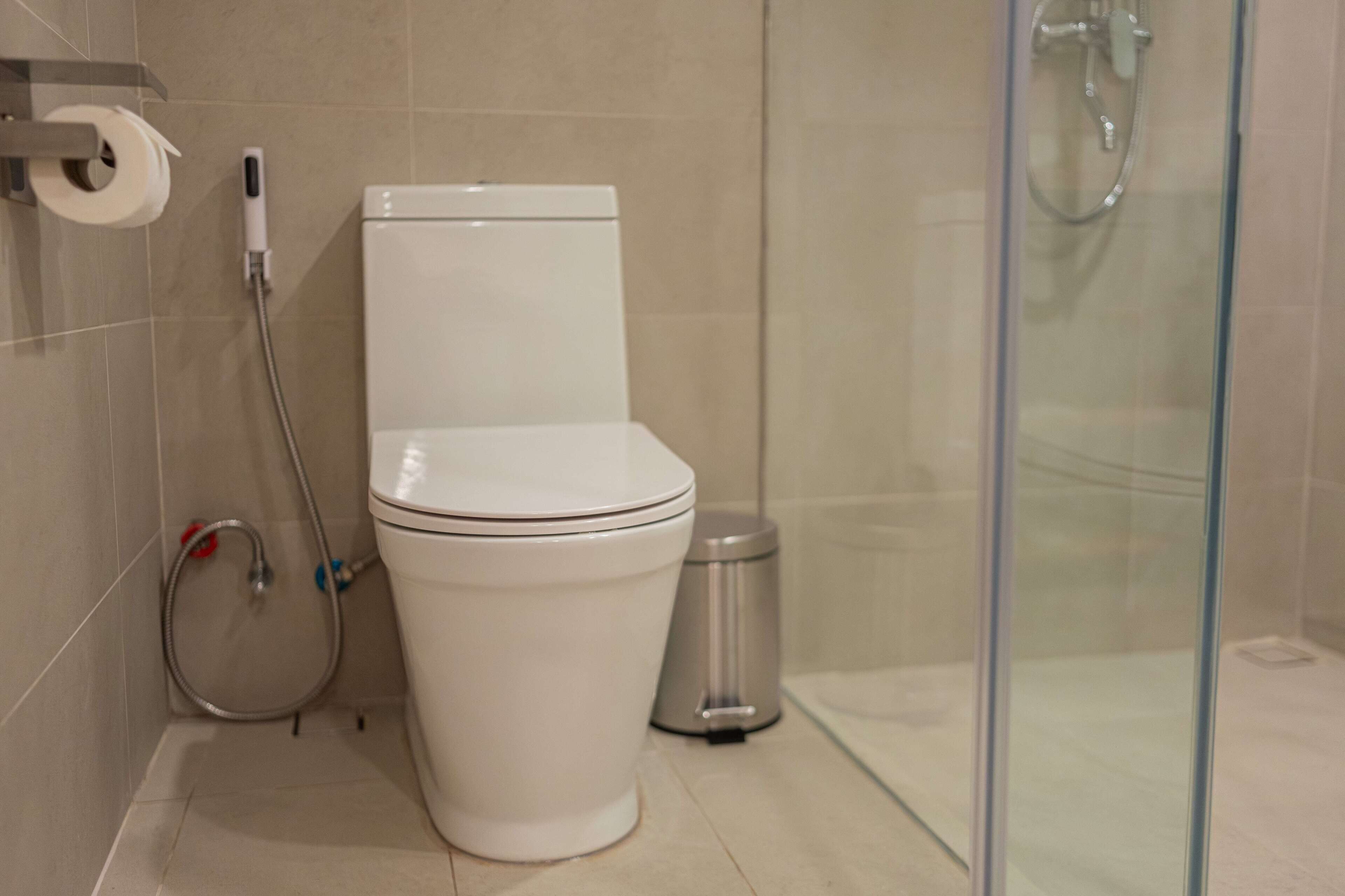 A bathroom with a toilet, a glass shower enclosure, and a trash bin.