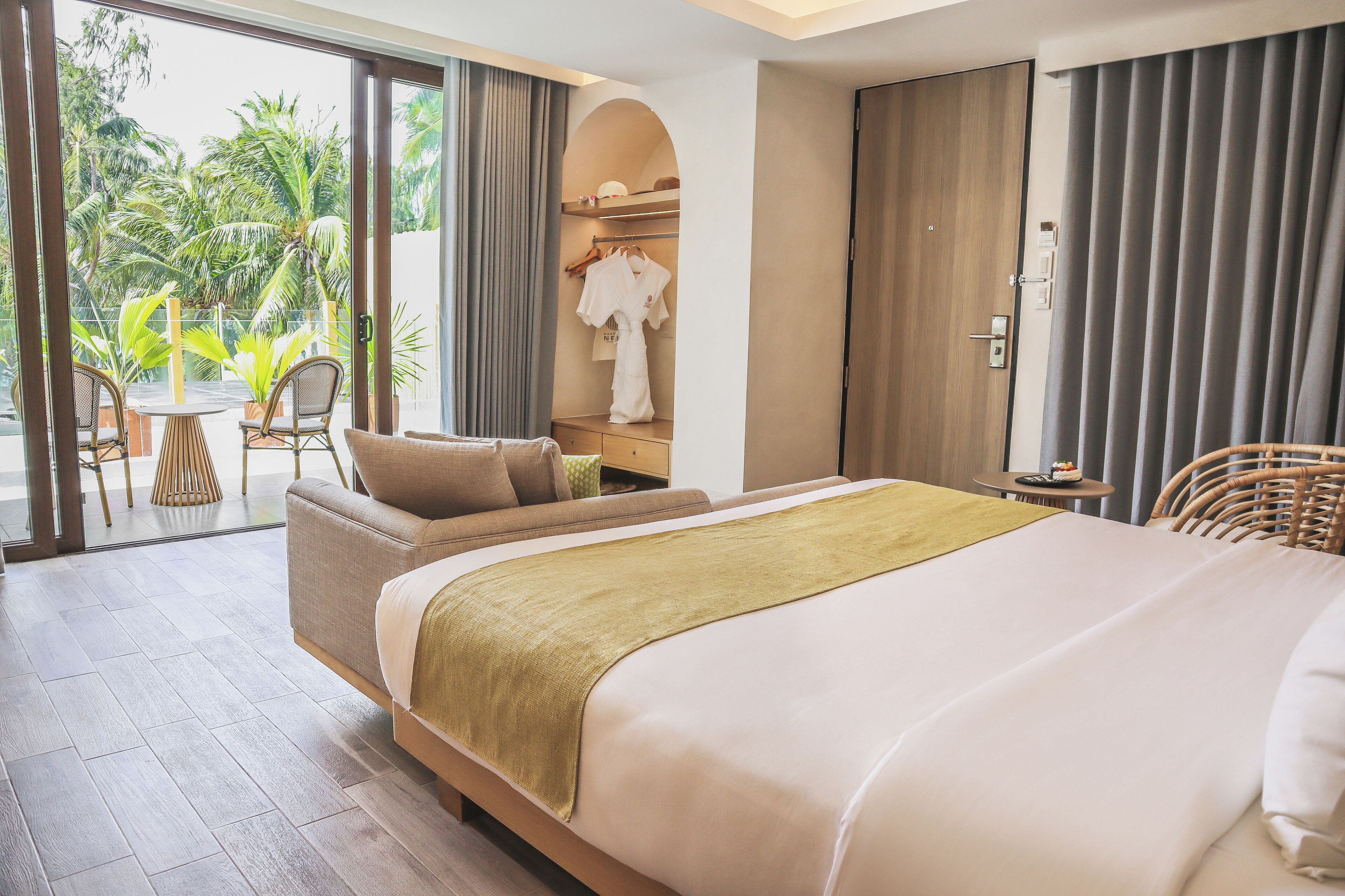 A hotel room with a large bed, a sofa, a dining table, and a view of palm trees.