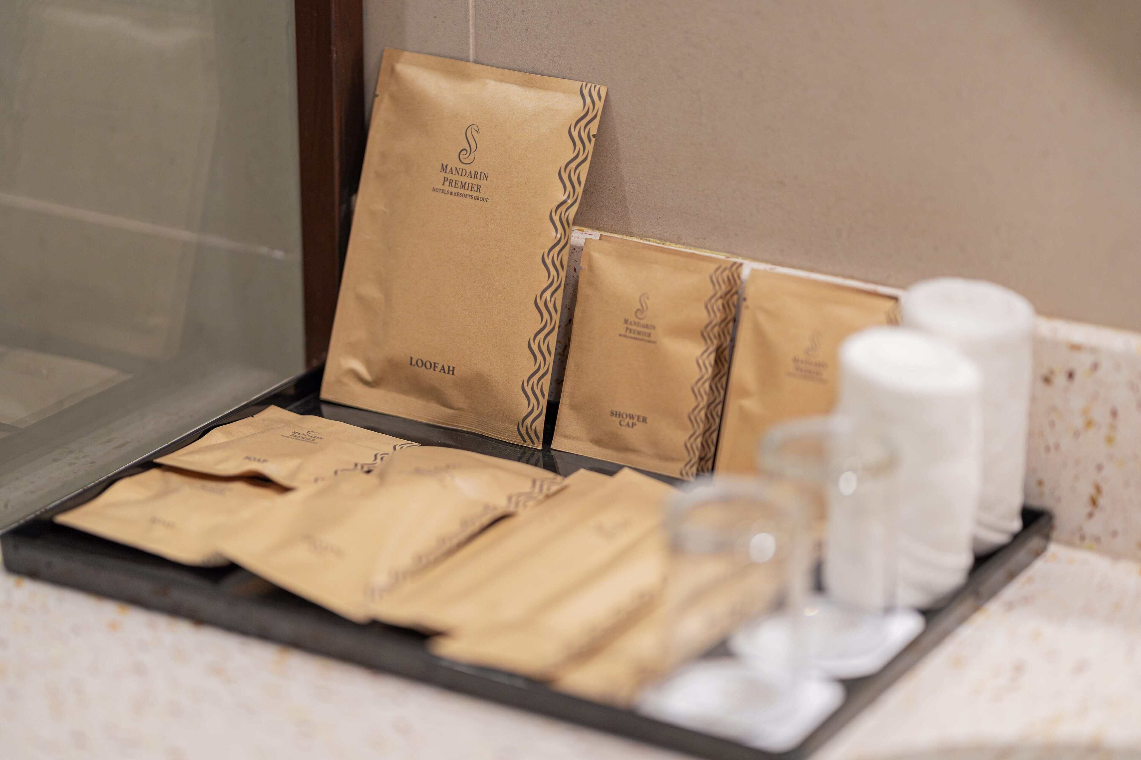 A tray with brown paper bags labeled 'Mandarin Premier' and 'Loofah', along with a glass and two white bottles, likely toiletries, on a hotel counter.