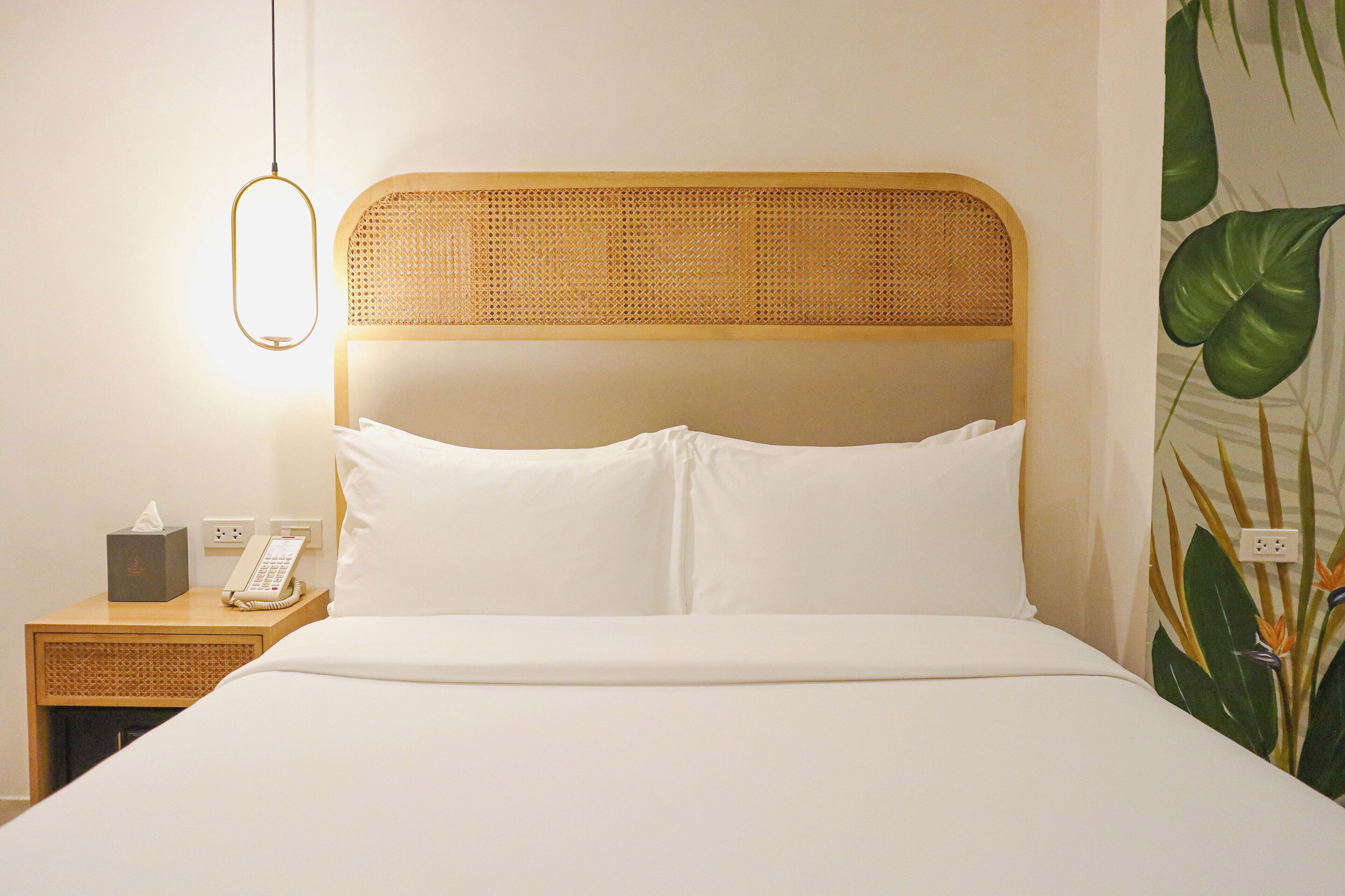 Una cama bien hecha con sábanas blancas, cabecera de madera, mesita de noche con lámpara y teléfono.