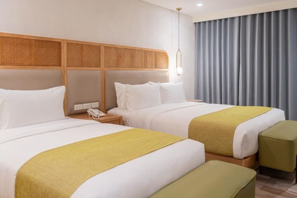 Een hotelkamer met twee bedden, een houten hoofdeinde, een nachtkastje met een telefoon en een raam met gordijnen.