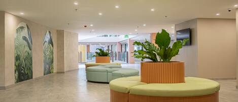 A spacious lobby with a curved wooden bench, potted plants, and a flat-screen TV mounted on the wall.