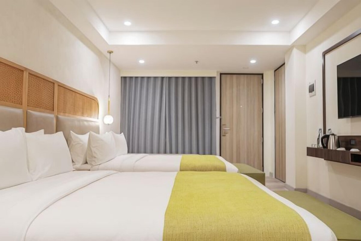 Quarto de hotel com duas camas, televisão, espelho e porta para o banheiro.