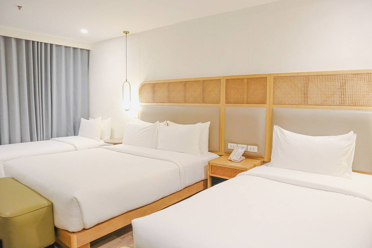 Een hotelkamer met twee bedden, een nachtkastje met telefoon en een groot raam met gordijnen.