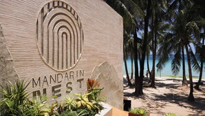 Ein Schild mit der Aufschrift 'MANDARIN REST' und ein Strand im Hintergrund, gesäumt von Palmen.